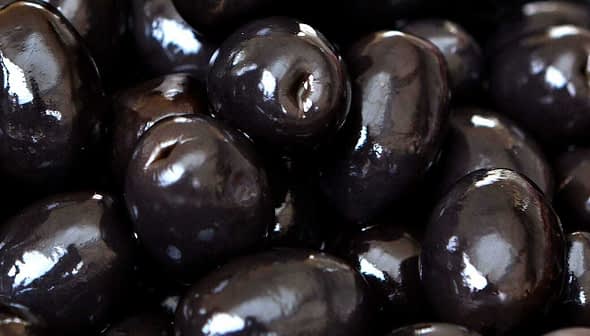 A close-up view of shiny black olives piled together in a cluster. - Olive Oil Times