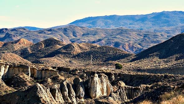 A panoramic view of a mountainous landscape featuring rolling hills and rocky terrain under a clear blue sky. - Olive Oil Times