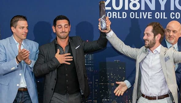 Four men at the 2018 New York Olive Oil Competition, one holding an award while others applaud. - Olive Oil Times