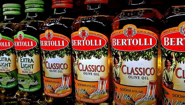 Row of Bertolli olive oil bottles in various types including Classico and Extra Light. - Olive Oil Times