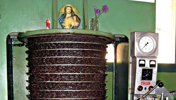 Olive oil pressing machine with a religious icon and flowers on top of it. - Olive Oil Times
