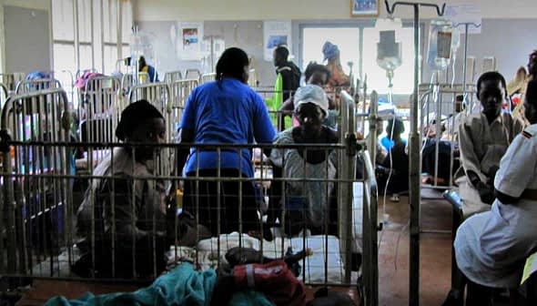 A hospital ward filled with patients in beds and medical staff attending to them. - Olive Oil Times