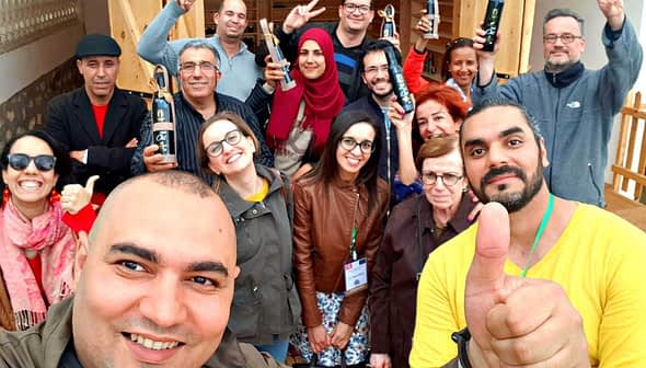 Group of people posing for a photo, some holding olive oil bottles, with smiles and gestures. - Olive Oil Times
