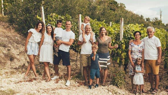 Group of people posing together in a vineyard with grapevines in the background. - Olive Oil Times