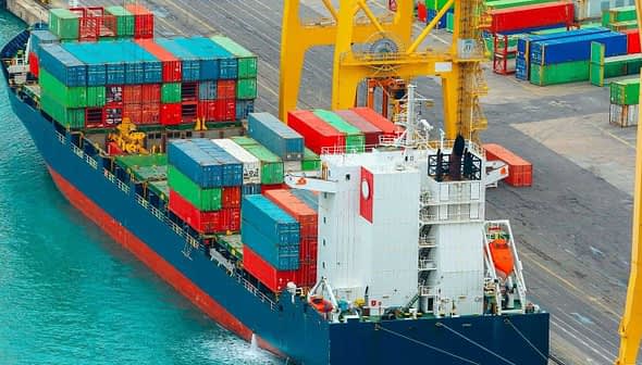 Cargo ship with colorful shipping containers docked at a port. - Olive Oil Times