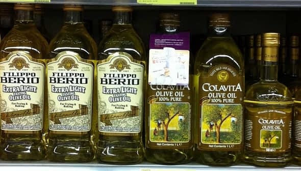 Various bottles of olive oil displayed on a supermarket shelf, including Filippo Berio and Colavita brands. - Olive Oil Times