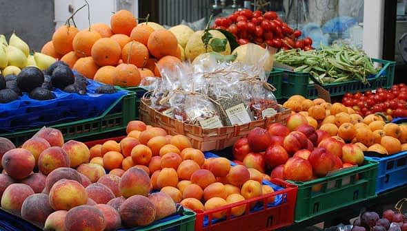 Assorted fresh fruits and vegetables displayed in crates at a market stall. - Olive Oil Times