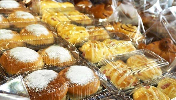 Various packaged bread products in clear plastic containers, including sweet rolls and pastries. - Olive Oil Times