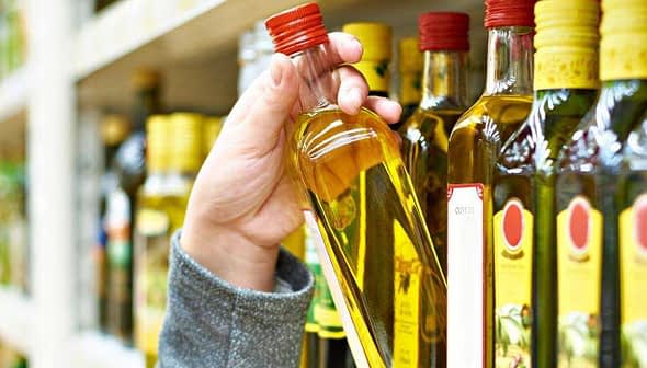 A person holding a bottle of olive oil from a shelf in a grocery store. - Olive Oil Times