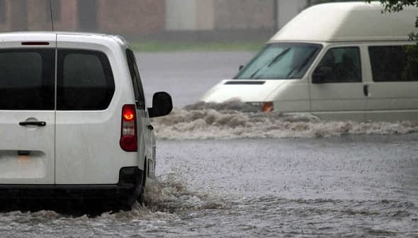 Two vehicles navigating through a flooded street during heavy rain. - Olive Oil Times