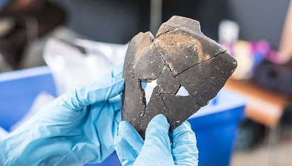 A person holding a fragment of a Celtic ceramic artifact with distinct shapes and textures. - Olive Oil Times