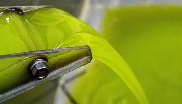 Stream of bright green extra virgin olive oil flowing from a mill spout into a container. - Olive Oil Times