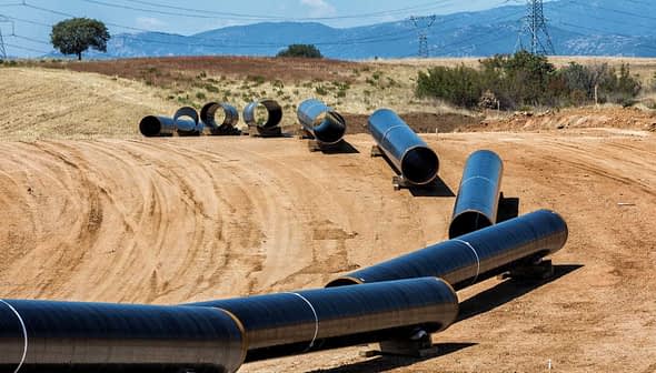 Several black pipeline sections laid out on a construction site with a dirt surface. - Olive Oil Times