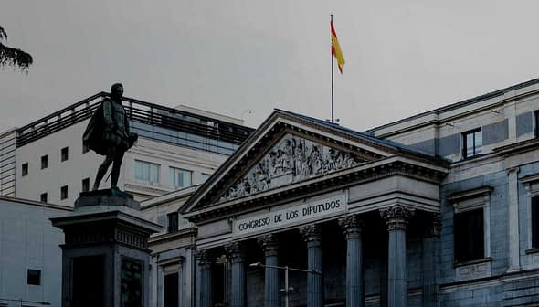 The Congreso de los Diputados building in Spain with a statue in front and a flag on top. - Olive Oil Times