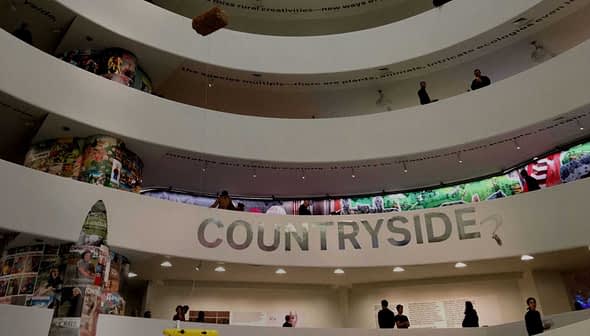 Interior view of a multi-level exhibition space with a large 'COUNTRYSIDE?' sign and visitors on different levels. - Olive Oil Times