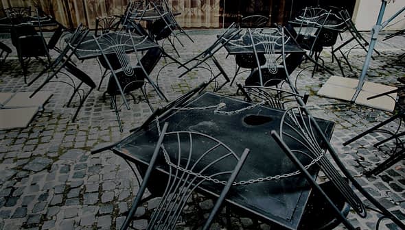 Several black metal tables and chairs stacked on a cobblestone surface. - Olive Oil Times