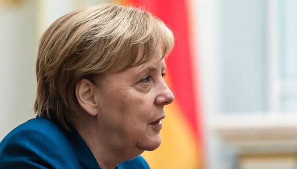 Profile view of Angela Merkel with short hair and a blue jacket, set against a blurred background. - Olive Oil Times