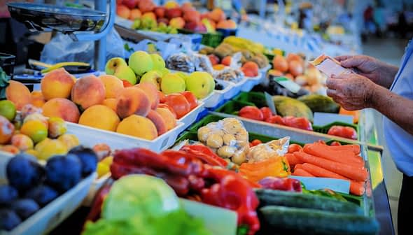 A selection of fresh fruits and vegetables displayed at a market stall, including peaches, carrots, and cucumbers. - Olive Oil Times