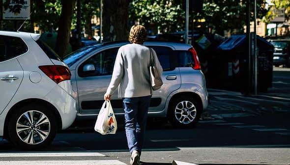 Individual walking on a street while carrying a grocery bag in one hand. - Olive Oil Times