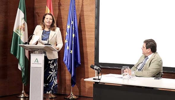 A woman presenting at a podium with flags of Spain and the European Union in the background. - Olive Oil Times