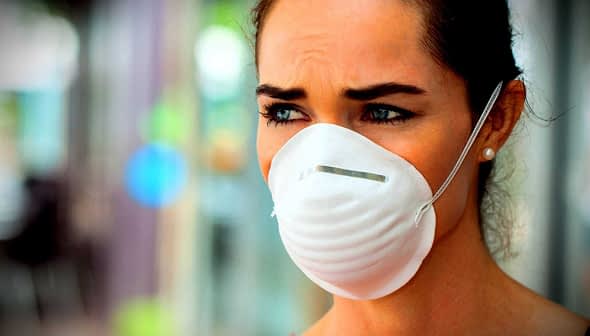 A woman with brown hair wearing a white face mask, looking serious with a neutral expression. - Olive Oil Times