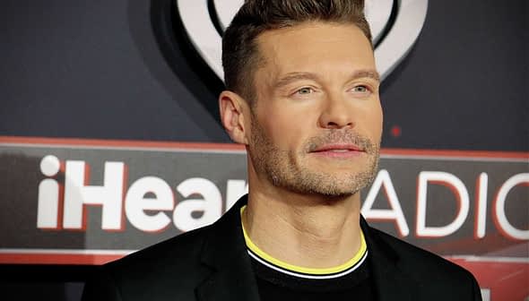 Man wearing a black suit with a yellow collar at an iHeartRadio event red carpet. - Olive Oil Times