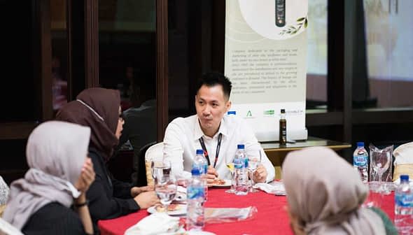 A man in a white shirt engaging in conversation with two women at a round table during a meeting. - Olive Oil Times