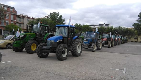 A row of agricultural tractors parked in a lot, featuring various colors and models. - Olive Oil Times