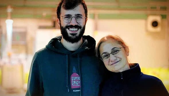 A man and a woman smiling while standing close to each other in a well-lit indoor setting. - Olive Oil Times