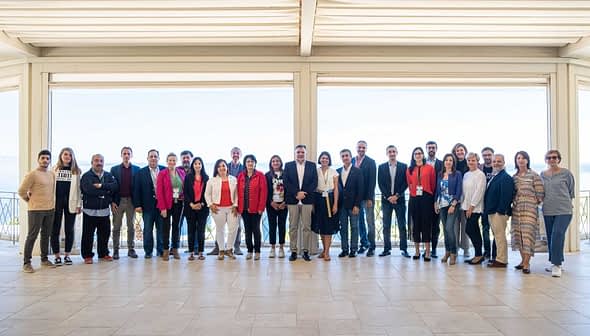 A group of individuals posing for a photo at an event, standing together in a spacious indoor area. - Olive Oil Times
