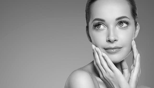 Black and white portrait of a woman with smooth skin and a thoughtful expression, gently touching her face. - Olive Oil Times