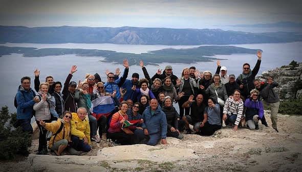 A large group of people posing together on a mountain with arms raised in celebration. - Olive Oil Times