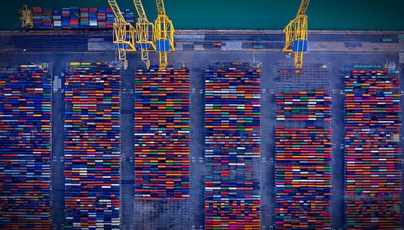 Aerial view of a shipping container yard filled with colorful containers arranged in rows. - Olive Oil Times