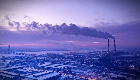Industrial power plant with smoke rising from tall chimneys against a twilight sky. - Olive Oil Times
