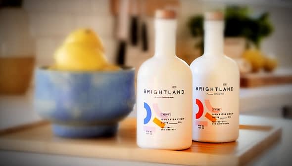 Two bottles of Brightland extra virgin olive oil with a blue bowl of lemons in the background. - Olive Oil Times