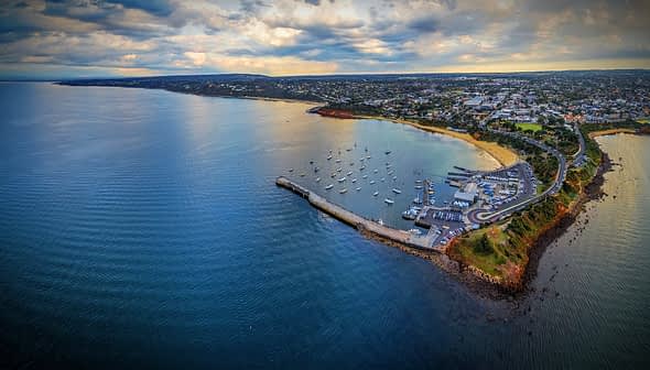 Aerial view of a coastal area featuring a harbor with boats and a shoreline. - Olive Oil Times