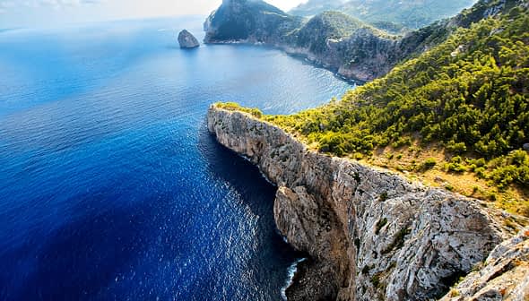 Aerial view of rocky cliffs meeting the blue ocean under a clear sky. - Olive Oil Times