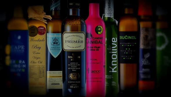 A collection of olive oil bottles featuring different brands and designs on a dark background. - Olive Oil Times