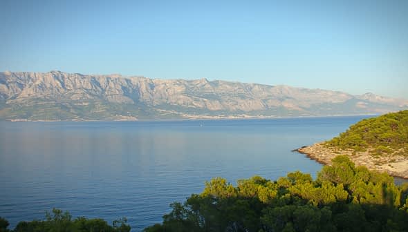 A coastal view featuring mountains in the background and calm water in the foreground. - Olive Oil Times