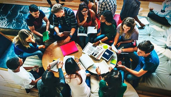 A diverse group of individuals gathered around a table, engaged in discussion with notebooks and materials. - Olive Oil Times