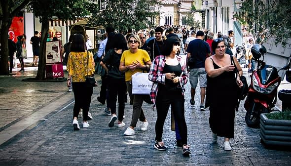 Group of people walking on a cobblestone street in an urban area with shops and trees. - Olive Oil Times
