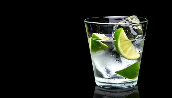 A glass filled with water, ice cubes, and lime wedges against a black background. - Olive Oil Times