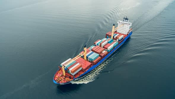 Aerial view of a container ship carrying colorful cargo containers on calm water. - Olive Oil Times