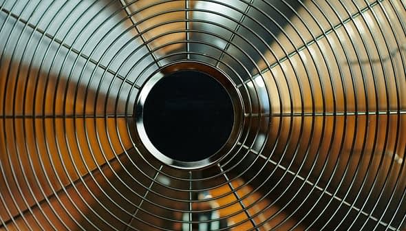 Close-up view of a metal oscillating fan with a wire grille and circular center. - Olive Oil Times