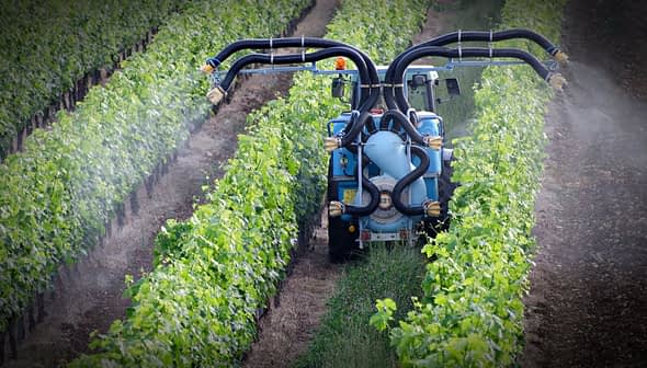 Tractor equipped with spraying apparatus working in a vineyard with rows of grapevines. - Olive Oil Times