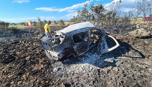 A burnt car surrounded by charred ground and sparse vegetation after a fire incident. - Olive Oil Times