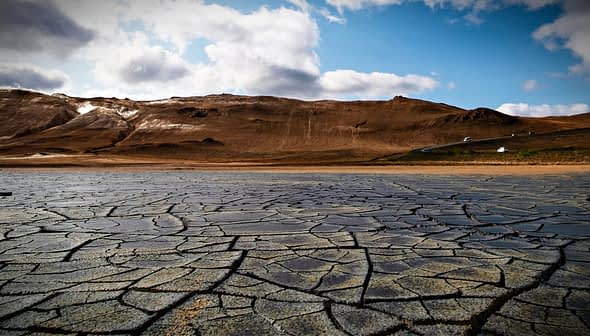 Dry, cracked earth surface with a mountainous background under a cloudy sky. - Olive Oil Times