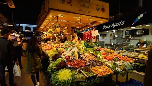 A vibrant market stall displaying a variety of fruits and vegetables, including greens, tomatoes, and grapes. - Olive Oil Times