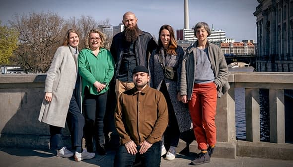 A group of six individuals posing together outdoors near a body of water. - Olive Oil Times