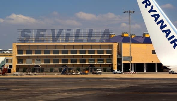 Sevilla airport building with the word 'SEVILLA' displayed prominently and a Ryanair airplane wing in the foreground. - Olive Oil Times